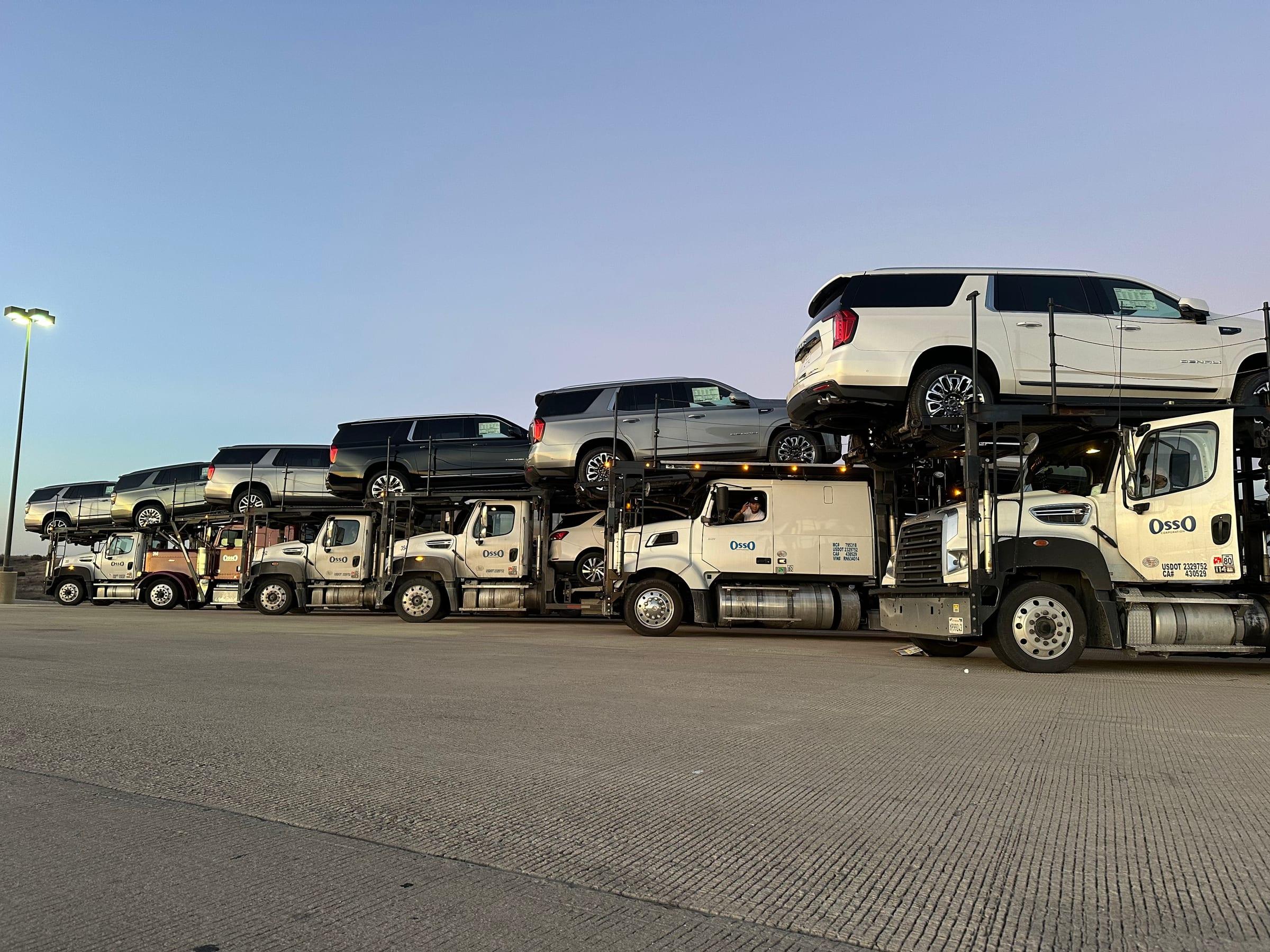 A line of Osso car haulers loaded with new SUVs at dusk